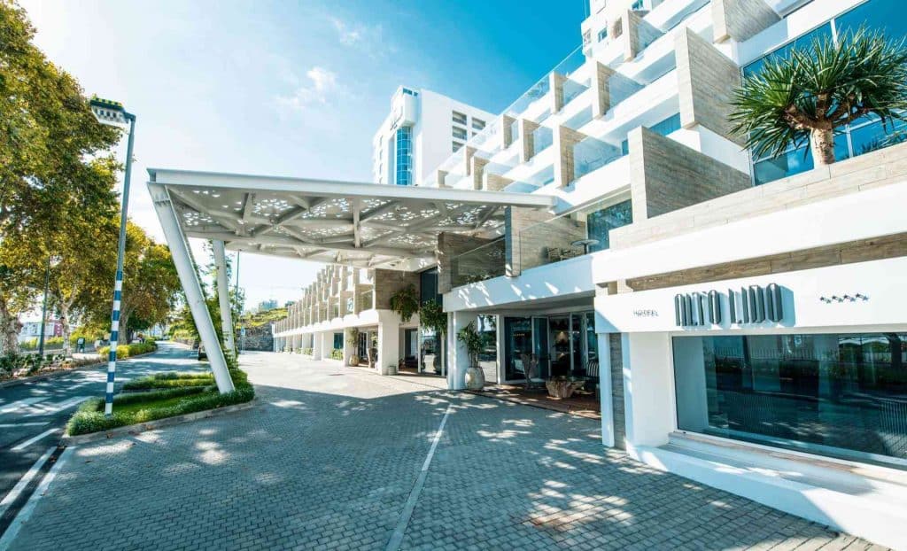 Moderner Hotelvordereingang mit Sonnenschutz, Glasfassade und umliegenden Bäumen.