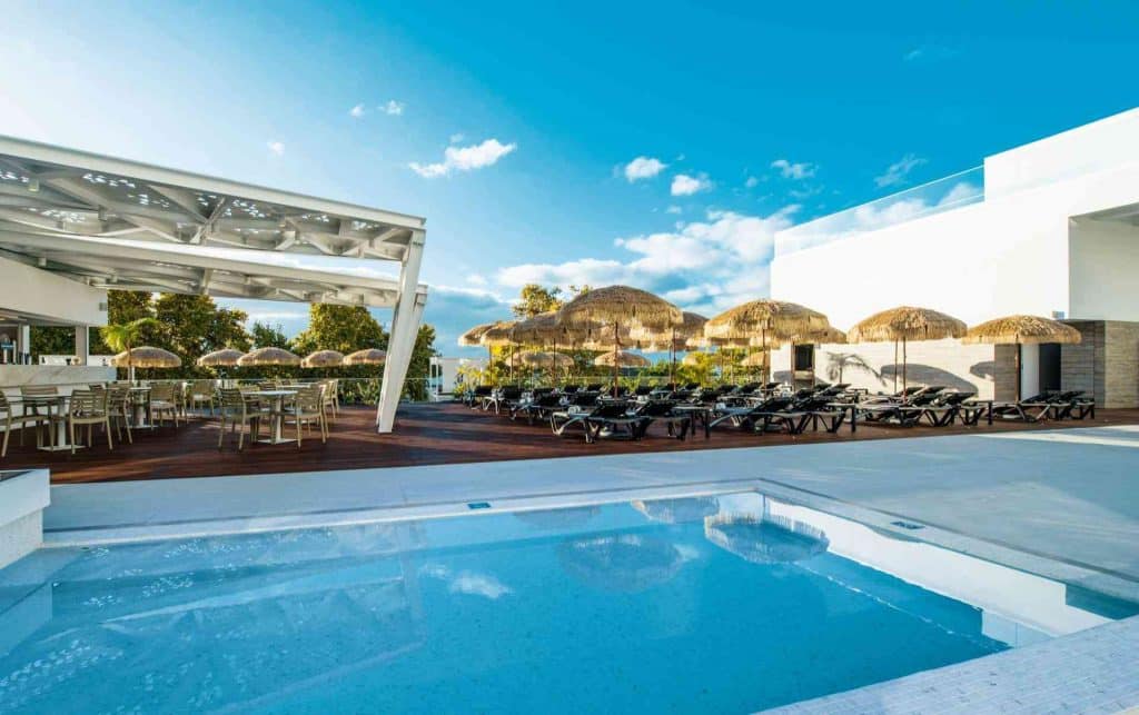 Moderner Außenpoolbereich mit Whirlpool, Liegestühlen und Sonnenschirmen unter blauem Himmel.